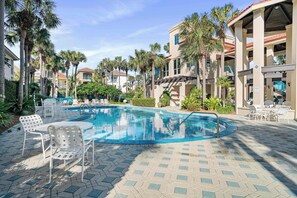A swimming pool with lounge chairs and a covered seating area, surrounded by palm trees and buildings. - Ocean Manor - 4 Bikes, Shared Pool, Pet Friendly! (Destin)