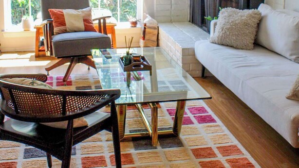 Uma sala de estar com uma mesa de centro de vidro, um sofá, uma poltrona, lareira e uma janela grande.