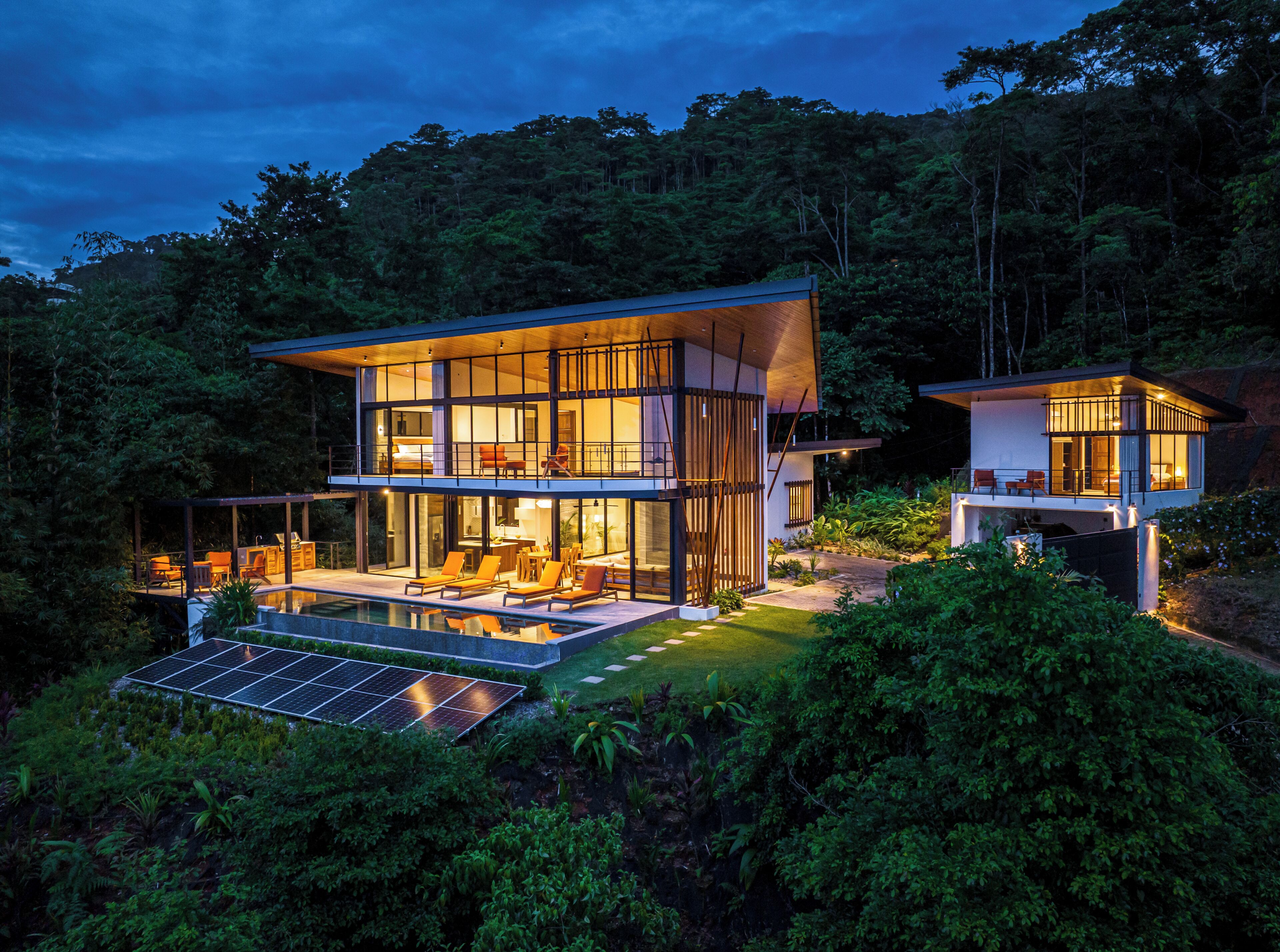 Ein modernes, zweistöckiges Haus mit Pool, umgeben von dichtem Wald.