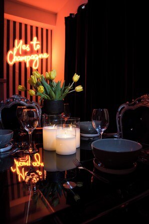 A table set for a meal with candles, a vase of yellow tulips, and a neon sign in the background. - Champagne Suite · Glam 2-Bed, Sleeps 4 · Central (Porthcawl)