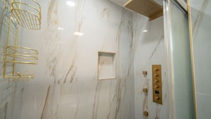 Ein Badezimmer mit Marmorwänden, einer Dusche mit Bedienfeld und goldenen Armaturen.