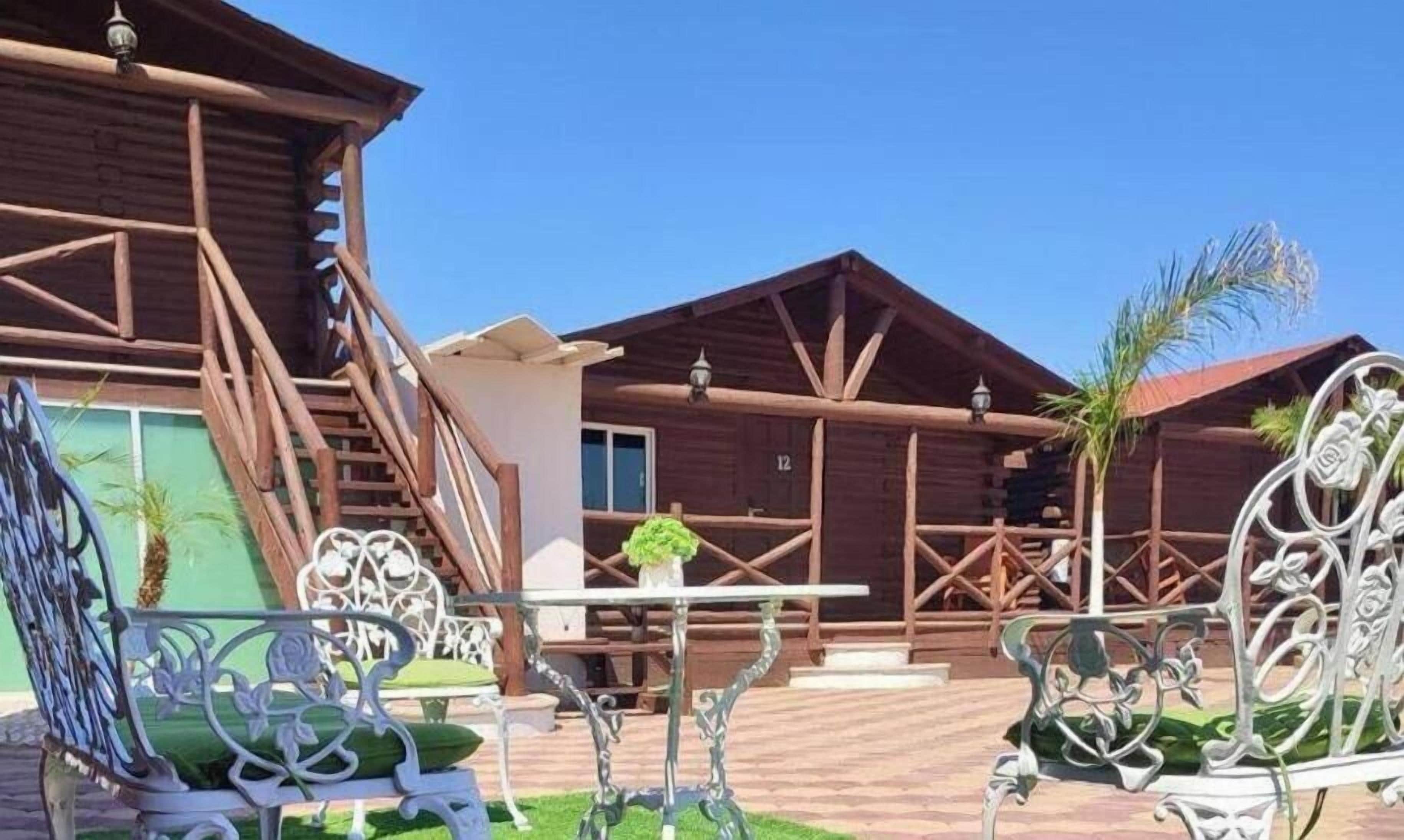 Un edificio de madera con una escalera, una mesa con una planta y sillas de metal ornamentadas.