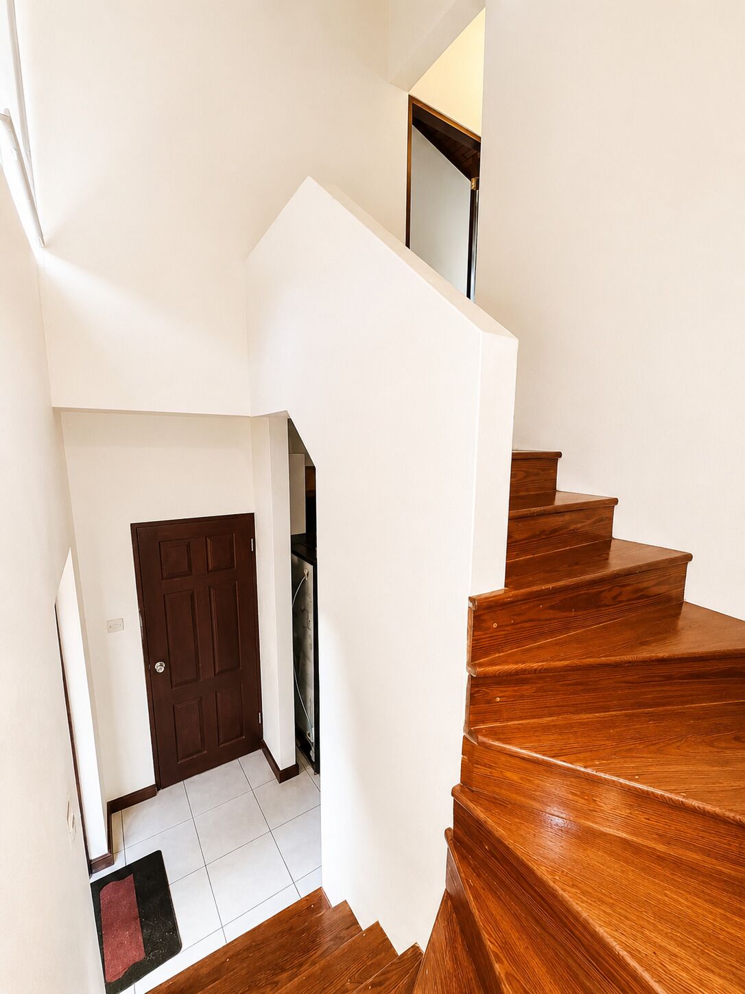 Una escalera que lleva a un segundo piso, una puerta de madera y una pequeña alfombra en el suelo.