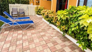 A building with a yellow exterior, a paved patio with blue lounge chairs, and a white fence. - Villa Augustas (Gros Islet)
