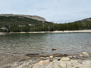 Ein ruhiger See mit steiniger Uferlinie, umgeben von dichtem Wald und Bergen.