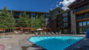 A swimming pool with lounge chairs and umbrellas, surrounded by multi-story buildings with balconies. - Juniper Springs Resort with Panoramic Views - Luxury Mountain Escape (Mammoth Lakes)
