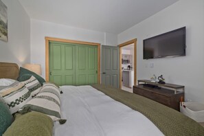 Ein Schlafzimmer mit einem Bett, einem Fernseher, einem Schreibtisch und einer grünen Tür.