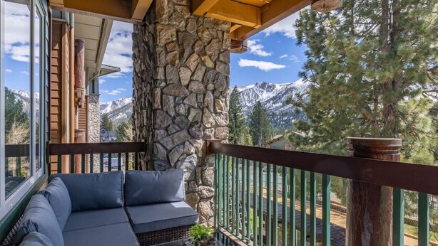 A balcony with a stone wall, a sofa, a table with drinks, and a view of mountains. - Juniper Springs Resort with Panoramic Views - Luxury Mountain Escape (Mammoth Lakes)