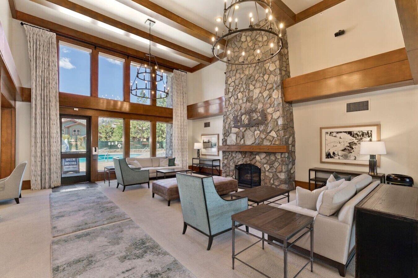 A spacious living room with a stone fireplace, large windows, and a pool view.