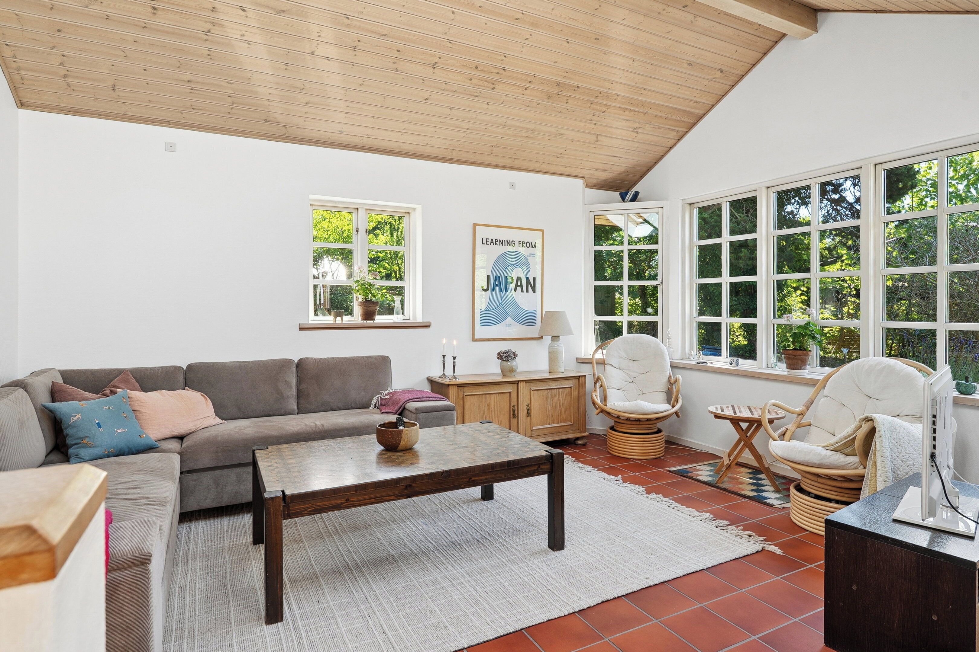 A living room with a sofa, coffee table, wicker chairs, a lamp, and a poster on the wall.