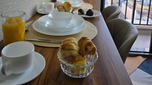 Een ontbijttafel met croissants, een glas sinaasappelsap en een bloemenvaas op een houten tafel.