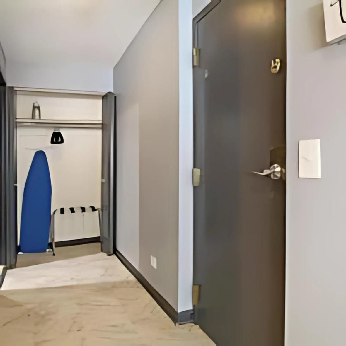 A hallway with a door, a blue surfboard, and a whiteboard on the wall.