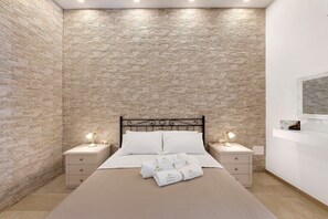 Een slaapkamer met een muur met een stenen patroon, een bed met witte lakens, twee nachtkastjes met lampen en een flatscreen televisie aan de muur bevestigd.
