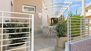 En innergård med en pergola, utomhusmöbler, krukväxter och ett tydligt synligt dörrnummer.