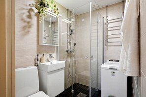 Ein modernes Badezimmer mit einer gläsernen Duschkabine, einem weißen Waschbecken und einem Handtuchhalter.