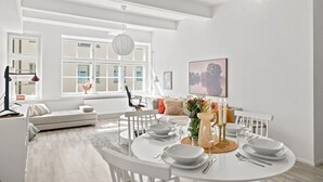 Ett modernt matområde med ett runt bord för fyra personer, en soffa och ett stort fönster som släpper in naturligt ljus.
