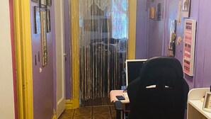 Ein Zimmer mit einem gemusterten Boden, einem schwarzen Bürostuhl, einem Schreibtisch mit Computer und einer Tür mit Vorhang.