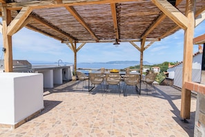 Un patio exterior con una parrilla, mesa de comedor y sillas, con vistas a un paisaje pintoresco.