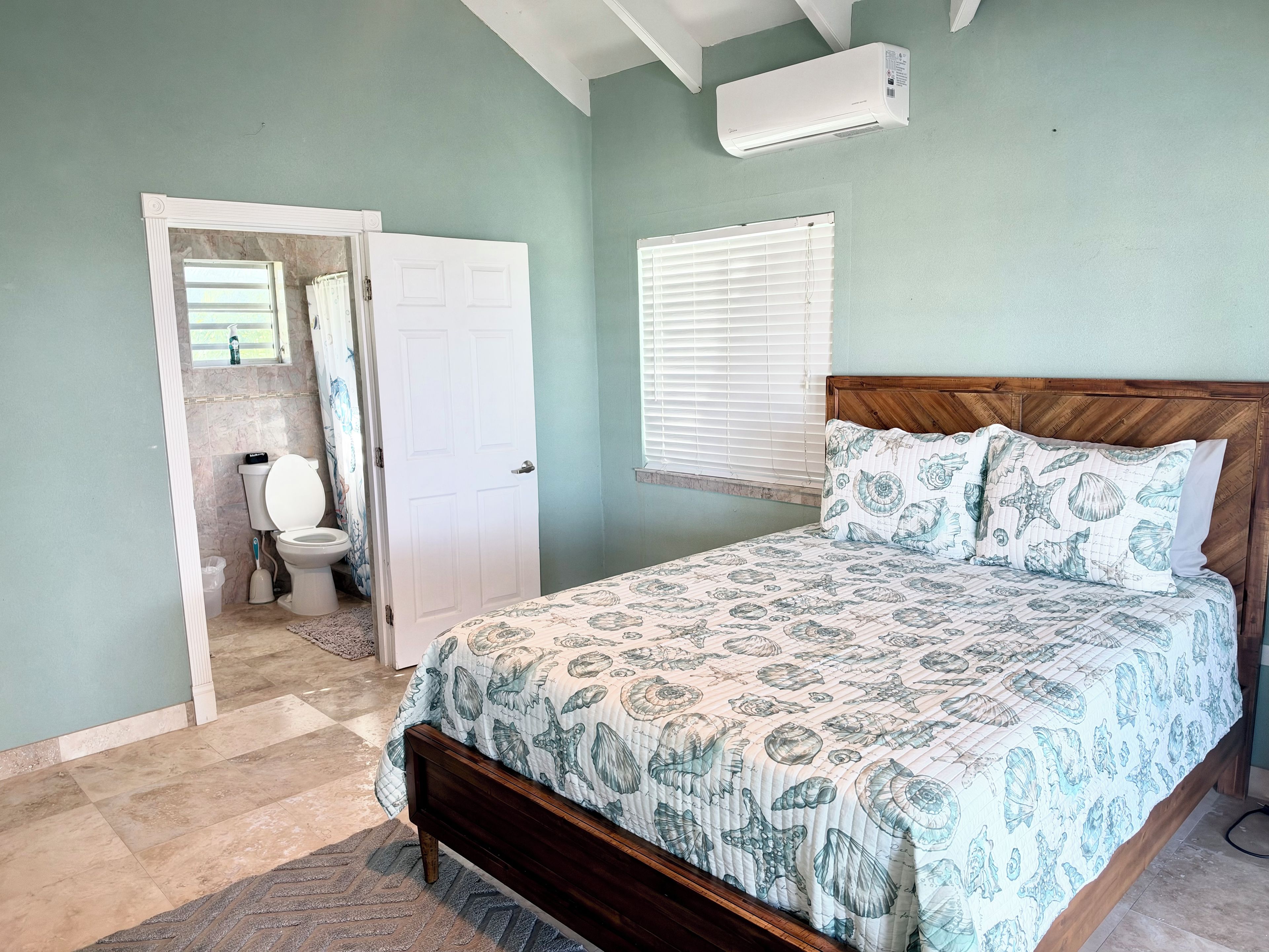 A bedroom with a bed, a door leading to a bathroom, and a window with blinds.