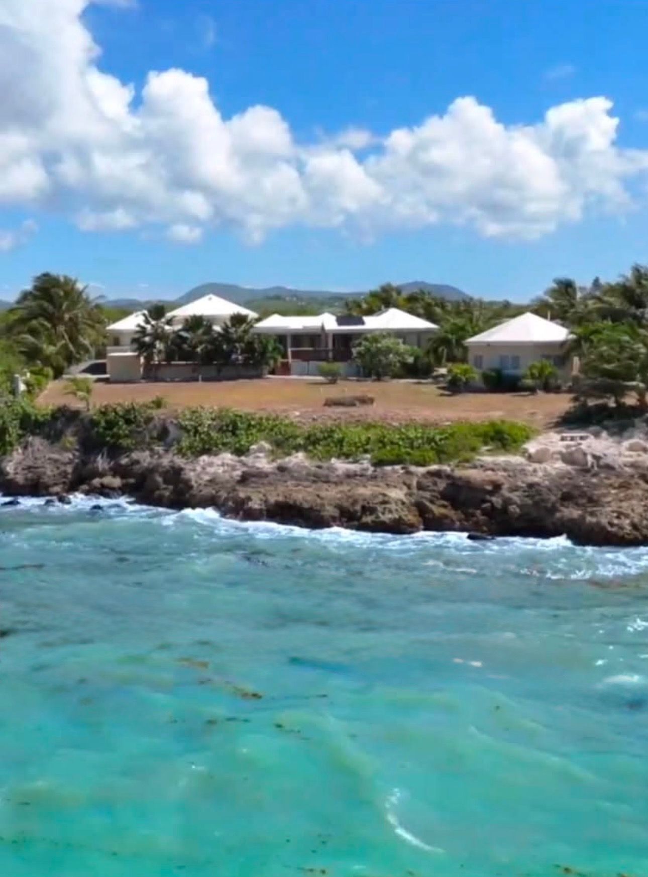 A coastal property with a rocky shoreline, clear turquoise waters, and a series of white-roofed buildings.