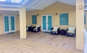 A covered outdoor seating area with cushioned chairs and a wooden deck.