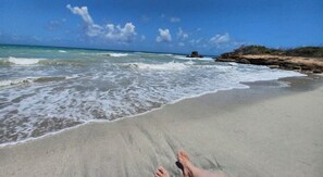 A beach with waves, a clear sky, and a rocky outcrop.