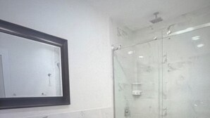 Ein Badezimmer mit weißem Waschbecken, einem Spiegel, einer Glasdusche und einer Toilette.