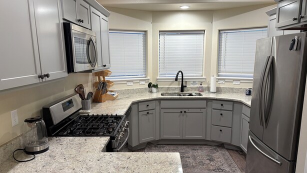 A kitchen with granite countertops, stainless steel appliances, and a corner sink.