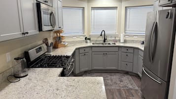 Cocina con encimeras de granito, electrodomésticos de acero inoxidable y un lavamanos en esquina.