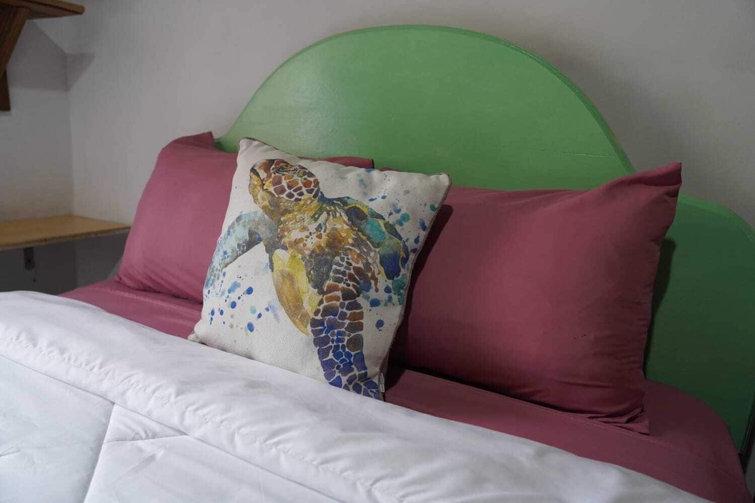A bed with a green headboard, white bedding, and a pillow with a mosaic sea turtle design.