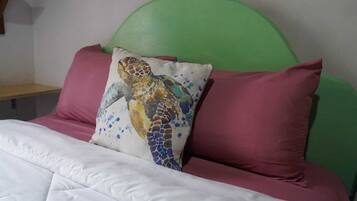 A bed with a green headboard, white bedding, and a pillow with a mosaic sea turtle design.