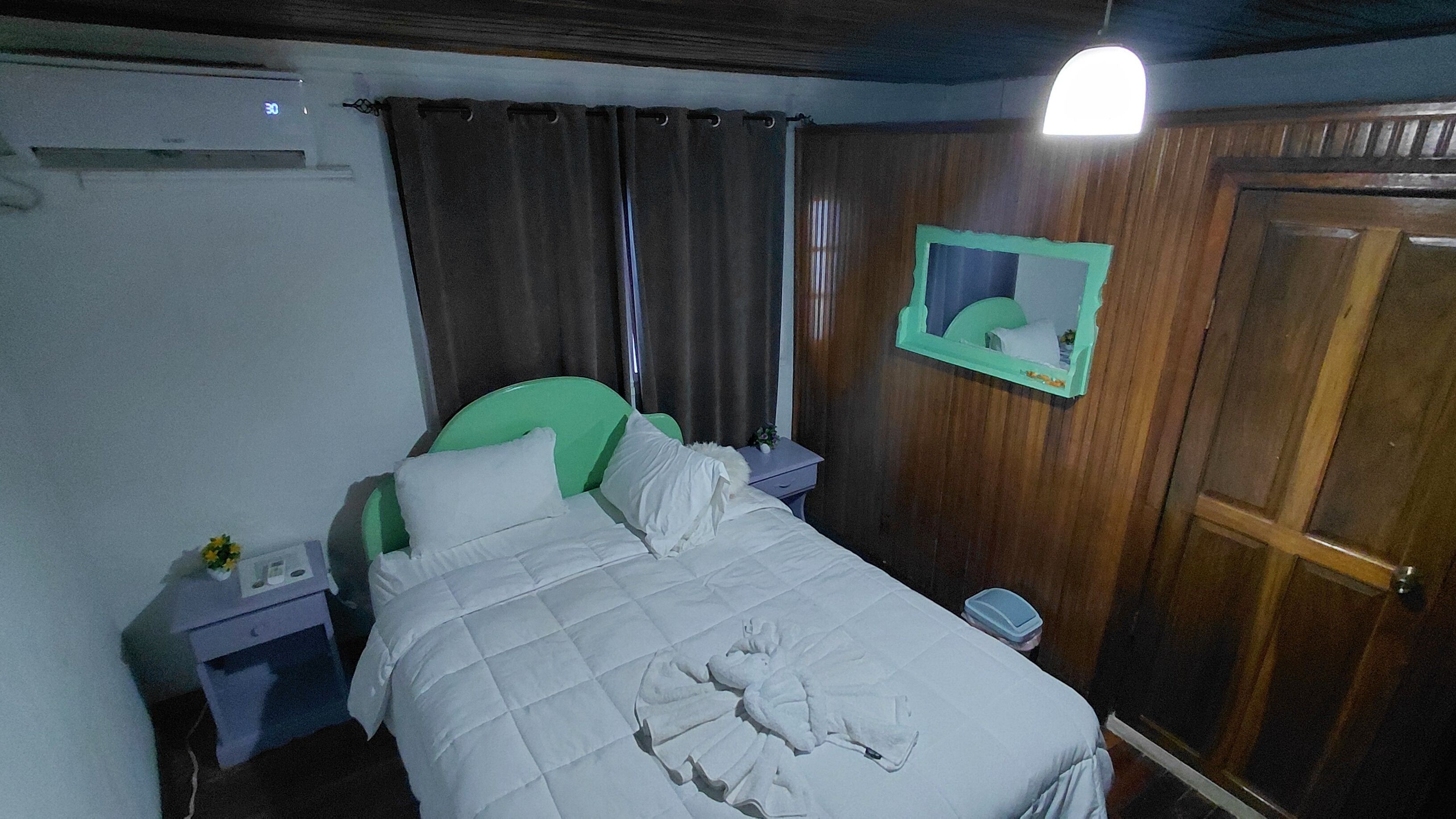 Une chambre à coucher comprenant un lit, une table de chevet, un miroir et une armoire en bois.