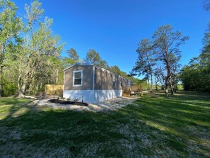 A single-story mobile home with a front porch, surrounded by trees and a grassy yard. - Freemans Landing Tickfaw River (Springfield)