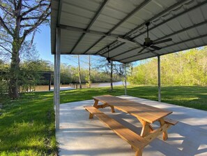 A covered picnic table with benches, a metal roof, and a grassy area with trees. - Freemans Landing Tickfaw River (Springfield)