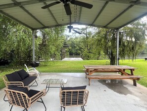 An outdoor patio with wicker furniture, a table, and a ceiling fan. - Freemans Landing Tickfaw River (Springfield)
