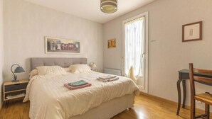 Une chambre à coucher avec un lit, une table de chevet, une chaise, un bureau et une fenêtre avec des rideaux.