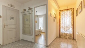 Un couloir avec une porte donnant sur une chambre, un radiateur et une fenêtre ornée de rideaux à motifs floraux.