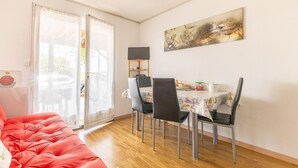 Une pièce avec un canapé rouge, une table à manger avec des chaises, un téléviseur posé sur un meuble et un tableau accroché au mur.