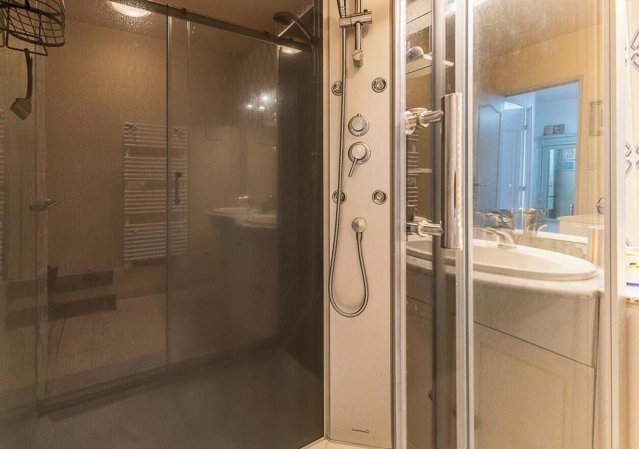 Een moderne badkamer met een douche met glazen wand, een zichtbaar toilet en een wastafel met spiegel.