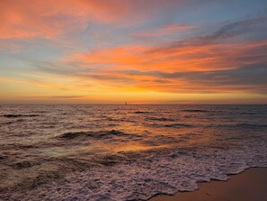 Una spiaggia con onde, una vela all'orizzonte e un cielo al tramonto.