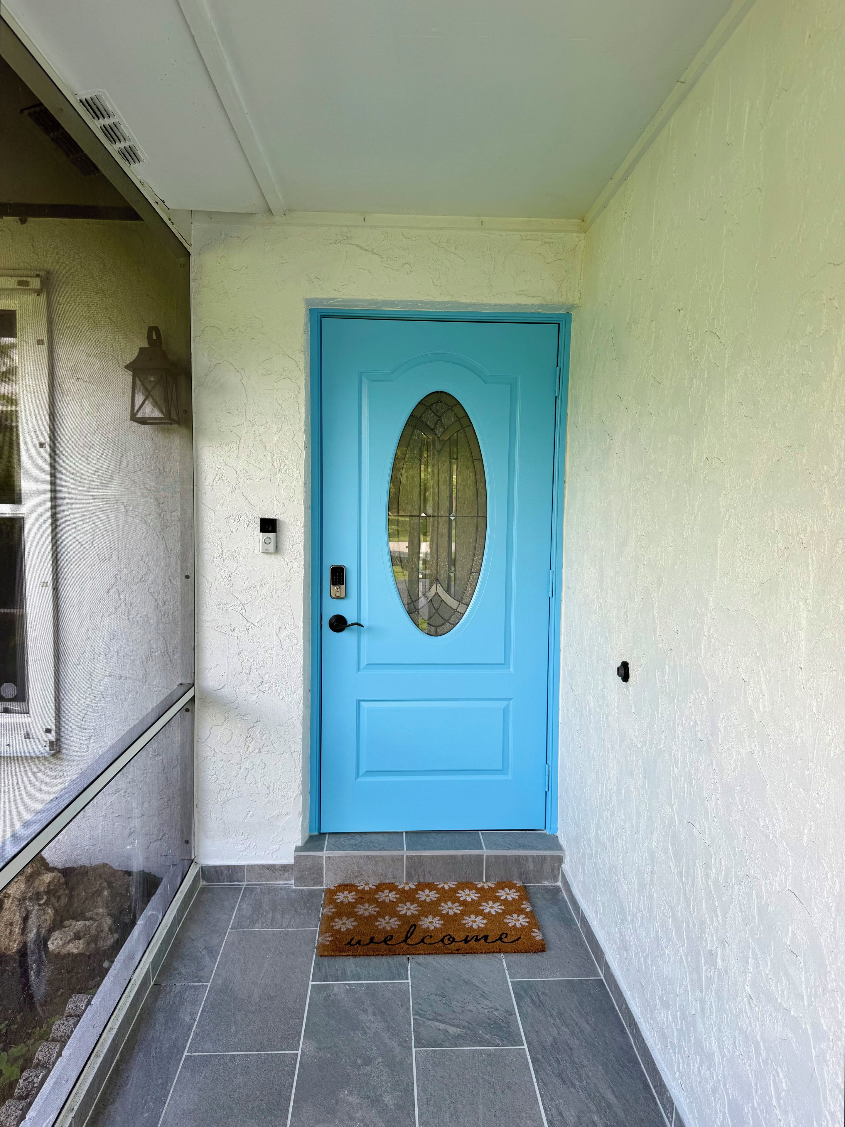 A blue door with a glass panel, a doormat with 'welcome' written on it, and a textured wall.
