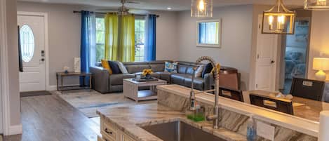 A modern kitchen with a marble countertop, a built-in sink, and a dining area with a table and chairs.