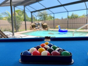 A pool table with a clear view of a backyard swimming pool and a fenced area. - Entire House with Seasonally Heated Pool and Waterfall in Naples (Naples)