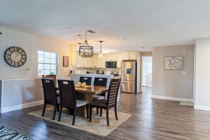 A modern kitchen with a dining area, featuring a clock, pendant lights, and a refrigerator. - Entire House with Seasonally Heated Pool and Waterfall in Naples (Naples)