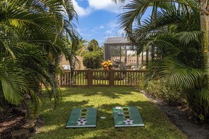 A backyard with two shuffleboard tables, a wooden fence, and a glass greenhouse structure. - Entire House with Seasonally Heated Pool and Waterfall in Naples (Naples)