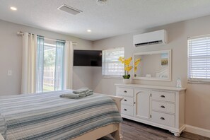 A bedroom with a bed, a dresser, a flat-screen TV, and a window with blinds. - Entire House with Seasonally Heated Pool and Waterfall in Naples (Naples)