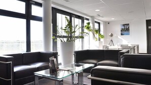 Un espacio de oficina moderno con sofás de cuero, una mesa de centro de vidrio y ventanas amplias.