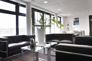Un espacio de oficina moderno con sofás de cuero, una mesa de centro de vidrio y ventanas amplias.