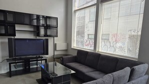 A living room with a flat-screen TV, a glass coffee table, a grey sofa, and a black entertainment unit. - Unique  loft like Apt with cache.. in 3 story small 3 unit warehouse conversion. (Montréal)