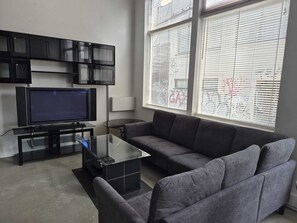 Ein Wohnzimmer mit Flachbildfernseher, einem Glastisch, einem grauen Sofa und einer schwarzen Unterhaltungsecke.